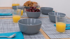 Un desayuno con tazones, vasos de zumo de naranja y croissants sobre una mesa con un mantel individual.