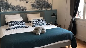 Un dormitorio con cama, mesita de noche, lámpara, un mural en la pared y ventana con cortinas.