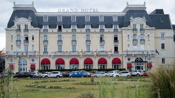 Un hotel grande de estilo arquitectónico europeo clásico, con múltiples balcones y una entrada central con toldos rojos.
