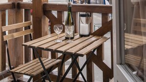 Una mesa de madera con una botella y un vaso, frente a una ventana que da a una calle con edificios.