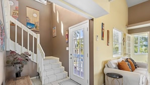 Un escalier menant à un palier avec une porte, un canapé blanc avec des coussins, une petite table ronde et une plante en pot.