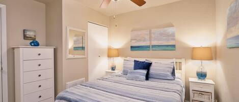 A bedroom with a bed, a ceiling fan, a dresser, and artwork on the walls.