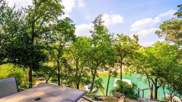 An outdoor seating area with a table and chairs, surrounded by trees and a view of a lake. - Incredible waterfront! Relaxing!- Swim & Fish, Pool Access (Point Venture)