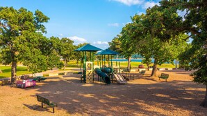 A playground with slides and swings, surrounded by trees and benches. - Incredible waterfront! Relaxing!- Swim & Fish, Pool Access (Point Venture)