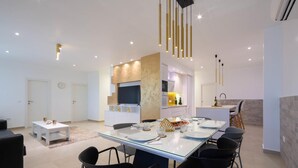 A modern living room with a glass dining table, black chairs, a white sofa, and a kitchen area with a microwave, oven, and sink. - Beach front apartment in Kastel Gomilica (Kastel Gomilica)