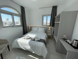 Quarto de hotel moderno com uma cama grande, duas mesas de cabeceira, uma escrivaninha com chaleira e vista para a cidade através das janelas.