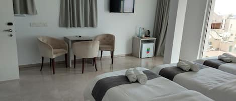 Habitación de hotel con dos camas, un escritorio, dos sillas, un minibar y un televisor en la pared.