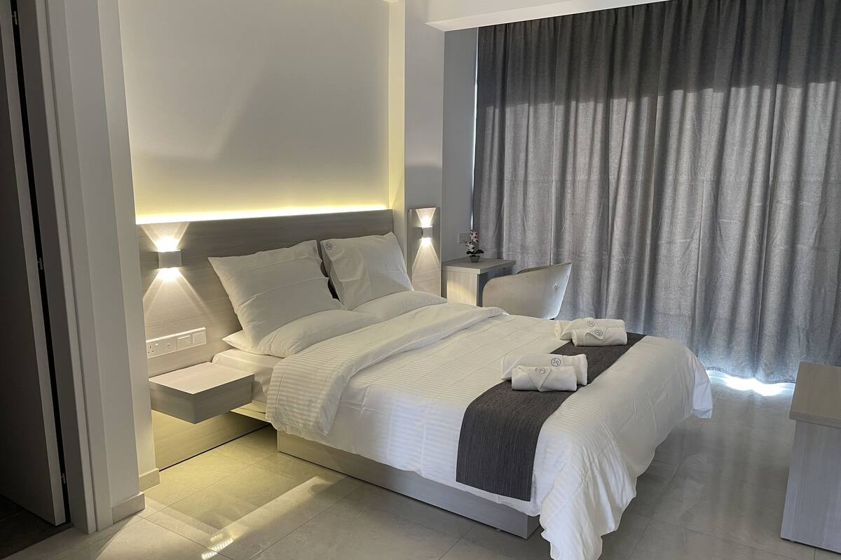 A modern hotel room with a large bed, bedside tables, a nightstand, and a window with curtains.