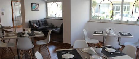 Un coin repas avec des tables disposées pour quatre personnes, des chaises blanches et un canapé en arrière-plan.