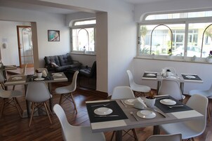 Un coin repas avec des tables disposées pour quatre personnes, des chaises blanches et un canapé en arrière-plan.