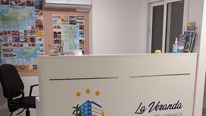Un espace d’accueil avec un comptoir de réception beige, un fauteuil de bureau noir et un sol carrelé.