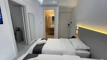 A hotel room with two beds, a bathroom, and a hallway leading to another room.
