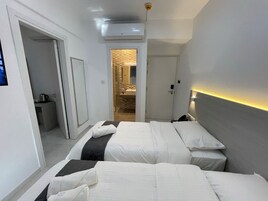 Habitación de hotel con dos camas, un baño y un pasillo que da a otra habitación.
