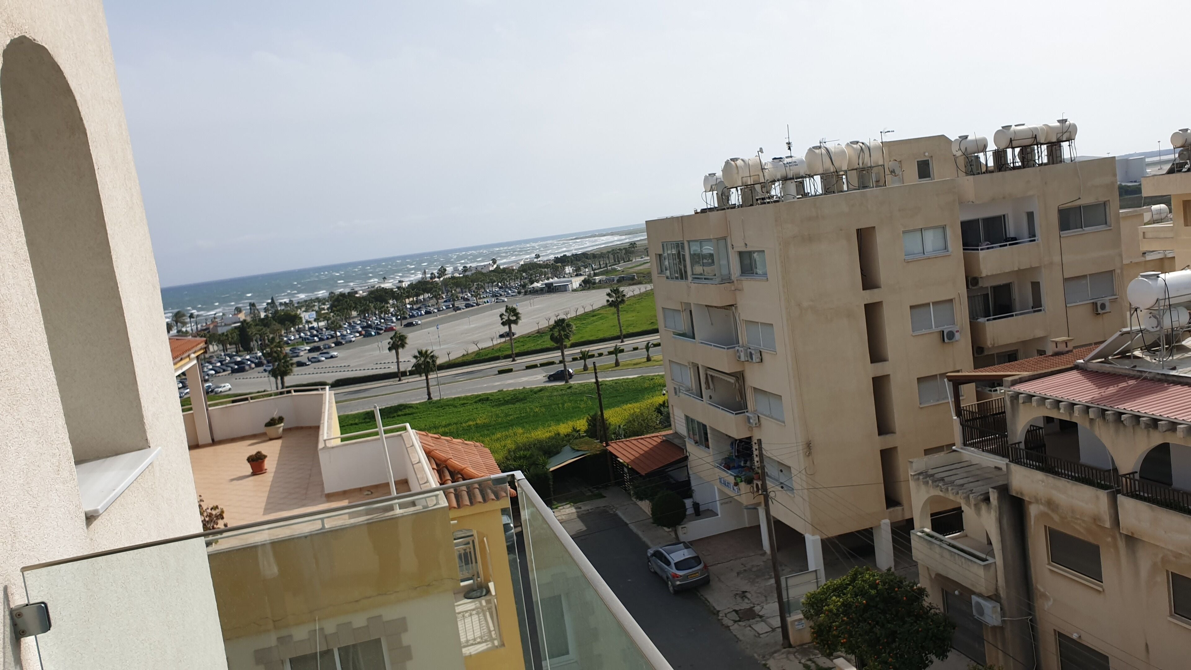 A residential building with multiple balconies, a view of the beach, and parked cars.