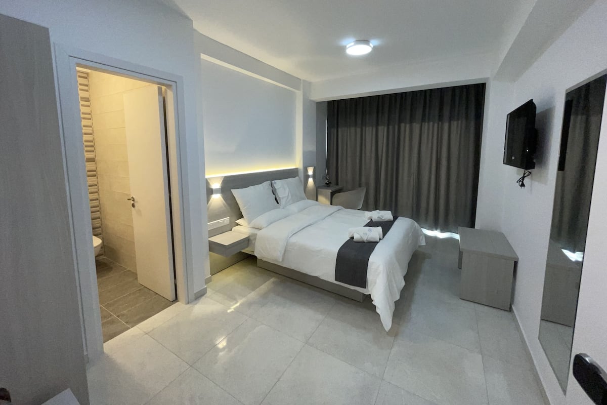 A modern hotel room with a bed, bedside tables, a TV, and a bathroom with a shower and toilet.