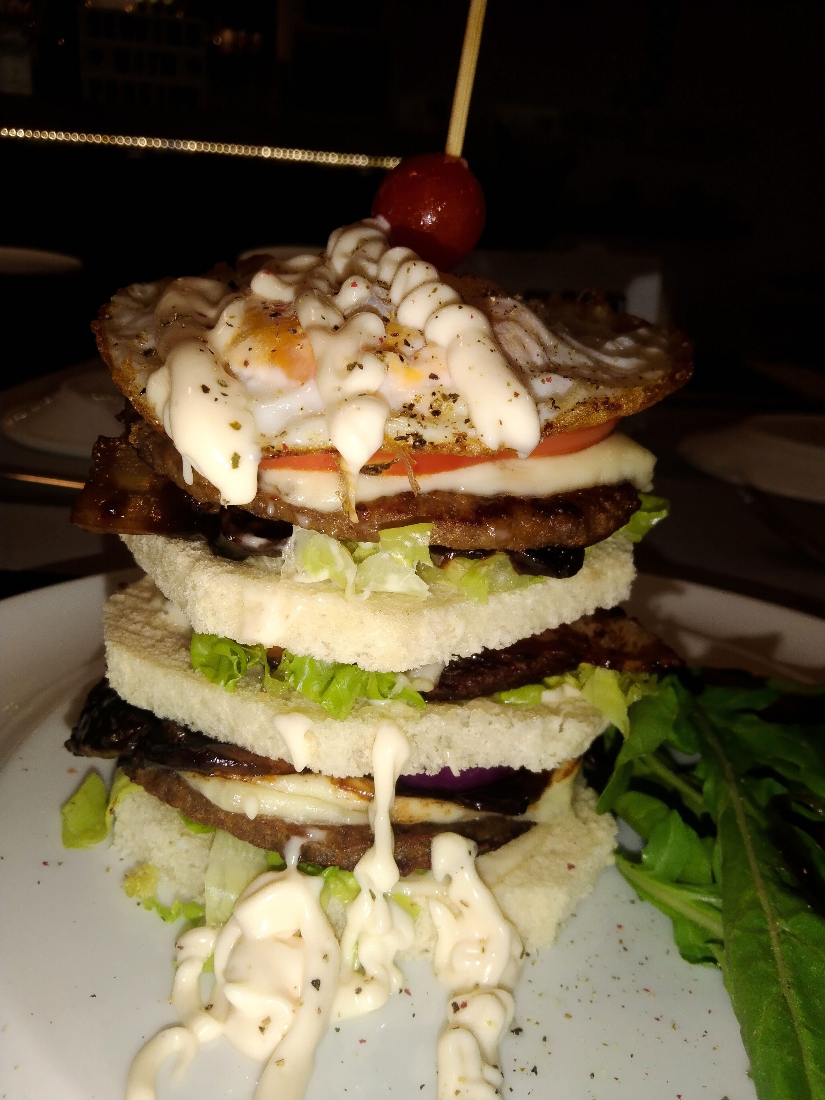 Un panino multistrato con diversi ingredienti e un pomodorino ciliegino in cima.