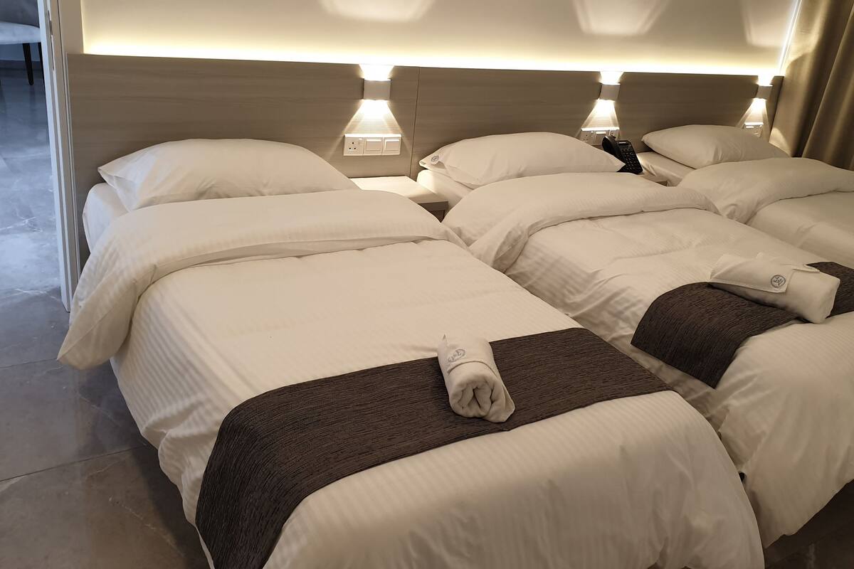 A hotel room with two beds, each with white linens and a brown throw blanket. There are bedside lamps and a remote control on one of the beds.