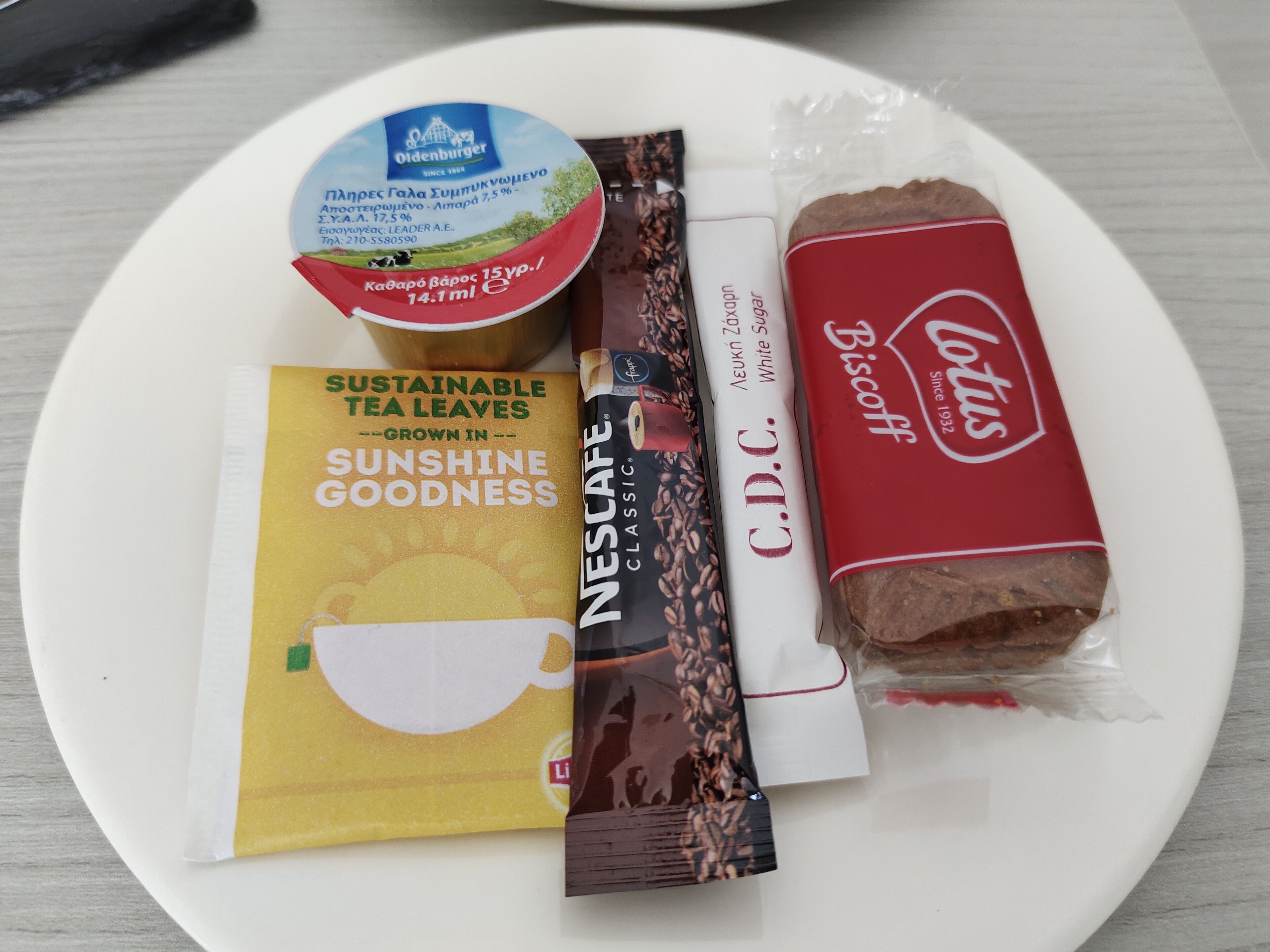 A plate with a yogurt cup, a tea bag, a biscuit, and a coffee creamer.