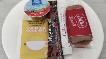 A plate with a yogurt cup, a tea bag, a biscuit, and a coffee creamer.