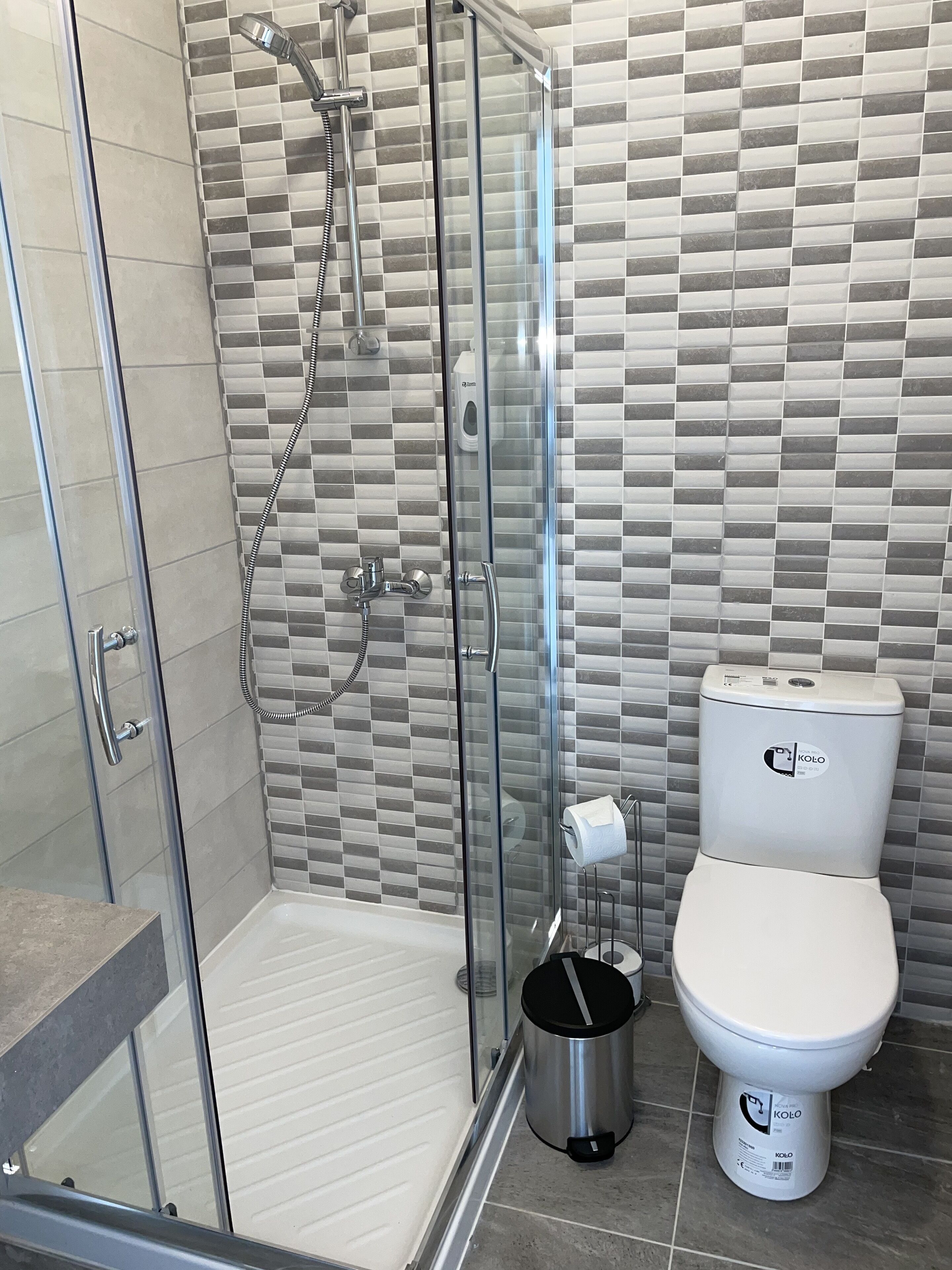 Une salle de bain moderne avec une douche à parois de verre, des toilettes et une poubelle.