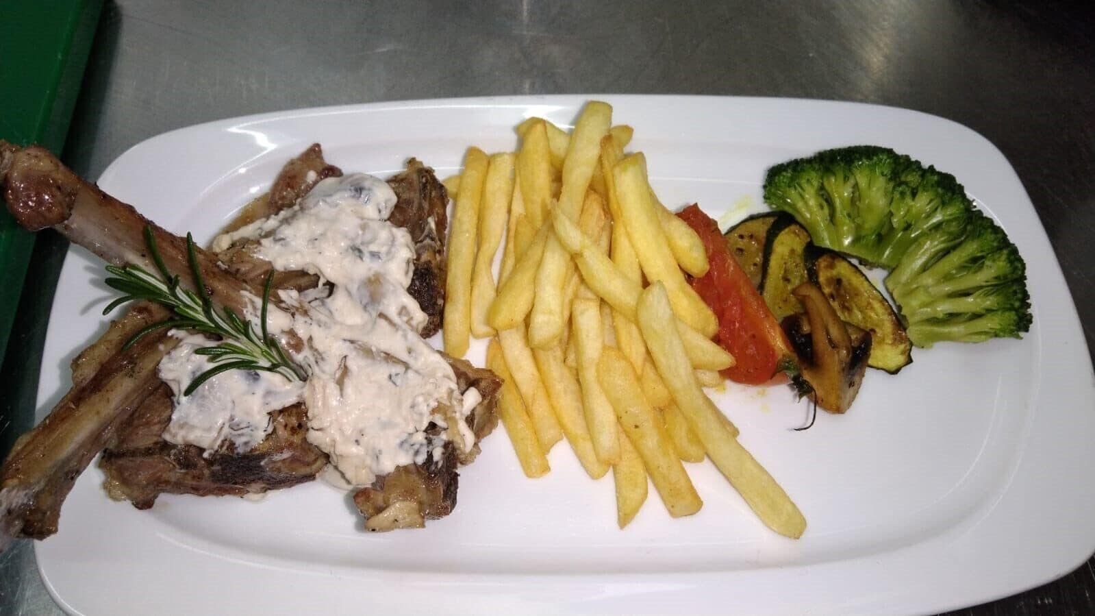A plate with a lamb shank, French fries, grilled vegetables, and a side of salad.