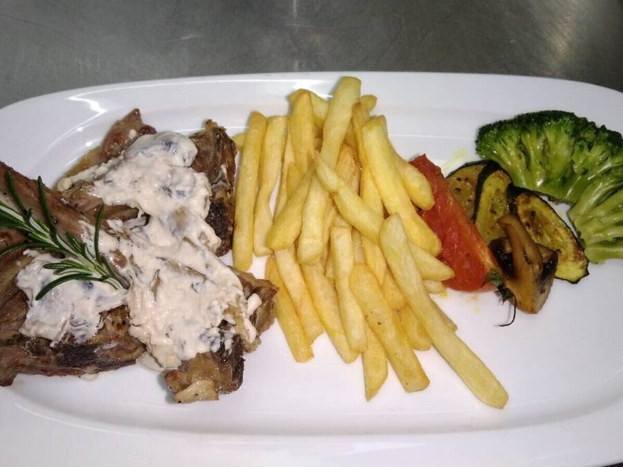 A plate with a lamb shank, French fries, grilled vegetables, and a side of salad.