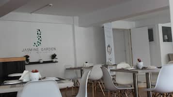 Un espace de restauration moderne avec des chaises et des tables blanches, une enseigne indiquant « Jasmine Garden Cafe - Restaurant », et une banderole décorative ornée d’un logo.