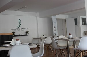 A modern dining area with white chairs and tables, a sign reading "Jasmine Garden Cafe - Restaurant", and a decorative banner with a logo.