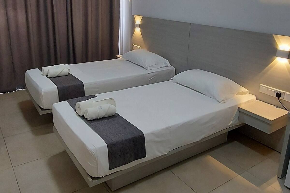 A hotel room with two beds, a nightstand, a lamp, and a ceiling light.