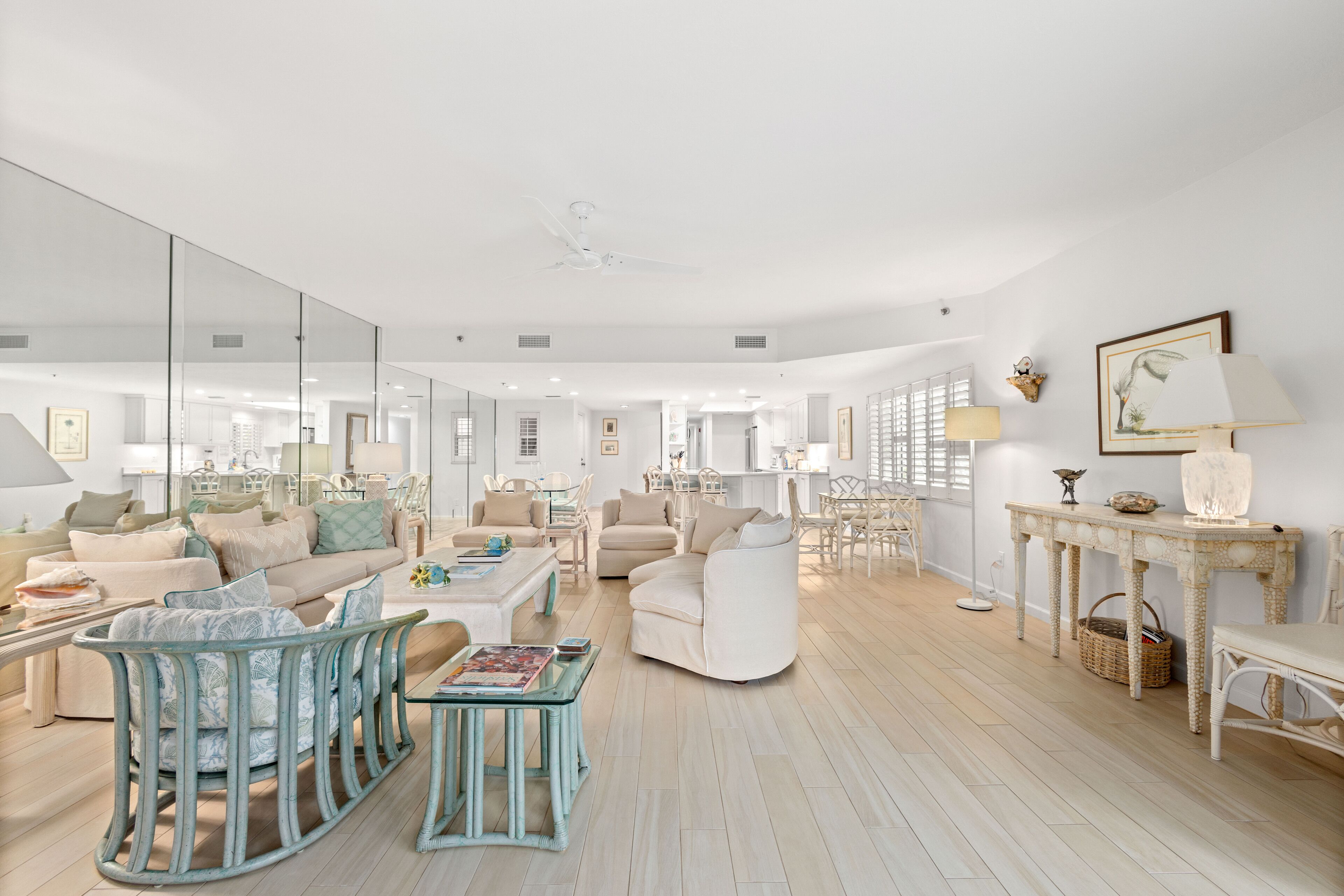 A spacious living room with a large mirror, a white sofa, a blue chair, and a dining table with chairs.