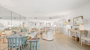 Un salon spacieux avec un grand miroir, un canapé blanc, un fauteuil bleu et une table à manger avec des chaises.
