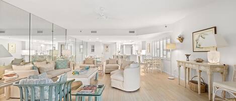 A spacious living room with a large mirror, a white sofa, a blue chair, and a dining table with chairs.