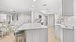 Une cuisine moderne avec des meubles blancs, un grand îlot central et un coin repas doté de chaises en osier.