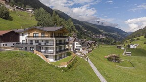 Un edificio moderno de varios pisos con balcones, ubicado en una ladera con vistas a un paisaje montañoso.