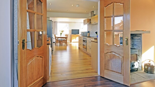 Una porta in legno che si apre su una cucina con un fornello, mobili e un'area pranzo con sedie.