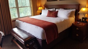 A hotel room with a large bed, two bedside lamps, a nightstand with a remote control, and a bench.