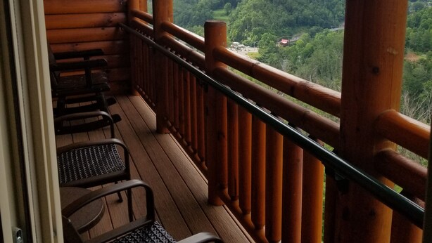 A wooden balcony with a metal railing overlooking a forested valley.