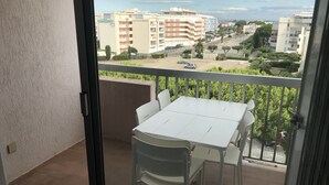 Un balcon avec une table et des chaises blanches, donnant sur un paysage urbain composé d’immeubles et d’une route.