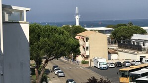 Une rue côtière bordée de voitures garées et d’un autobus, des immeubles dotés de balcons et un phare visible au loin.