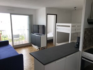 Kompakti huone, jossa on pieni keittiönurkkaus, sänky, televisio ja parveke, jossa on ulkokalusteita.