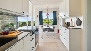 Una cocina moderna con armarios blancos, una zona de comedor con mesa y sillas, y vistas al exterior.
