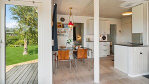 Una cocina moderna con armarios blancos, una mesa de comedor de madera y sillas. Se ve un jardín verde a través de una puerta abierta.