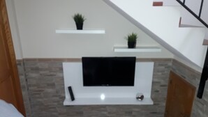 Una sala de estar con una televisión de pantalla plana montada en una pared blanca, una mesita y una silla.