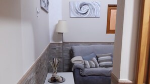Un espacio habitable compacto con un sofá gris, una mesita blanca con un adorno, una lámpara de pie y una pared con un diseño en espiral.