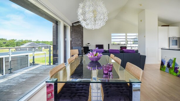 Een moderne eetruimte met een glazen tafel, rieten stoelen en een paars decoratiestuk.