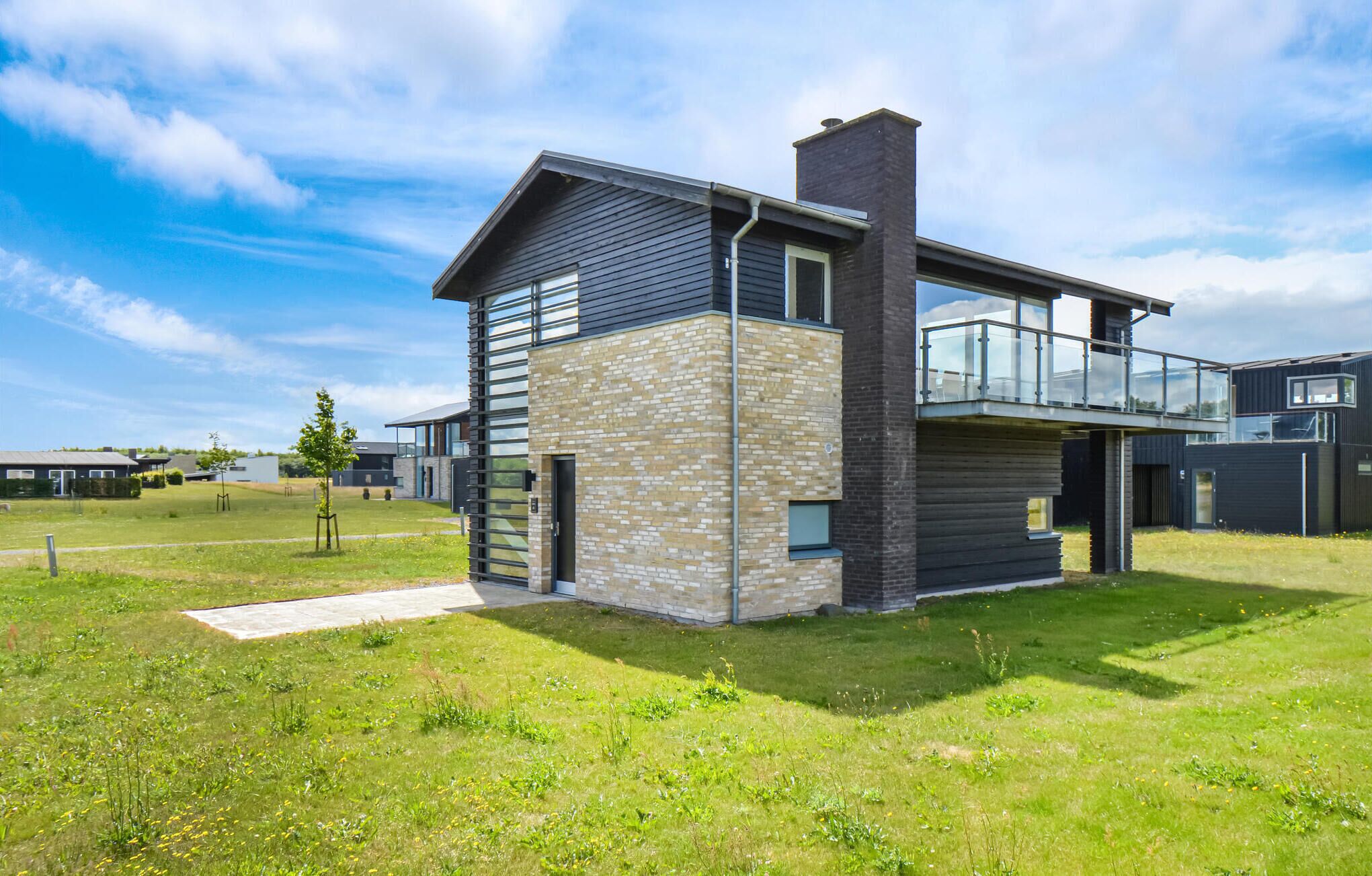 Une maison moderne à deux étages, dotée d’une façade en pierre, de grandes fenêtres et d’un balcon.