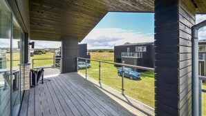 Een modern gebouw met een houten terras en uitzicht op een auto en een veld.