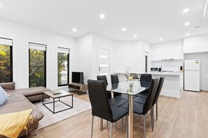 Een moderne woonkamer met een bank, salontafel en een eethoek met stoelen.
