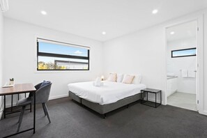 A modern bedroom with a bed, bedside table, and a desk with a chair. - Domi Rentals - The Hampton Homes (Moorabbin)