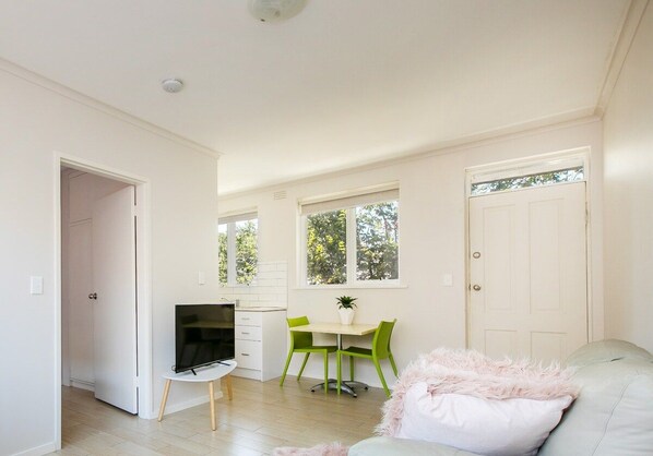 A modern living room with a flat-screen TV, a dining area with a table and chairs, and a sofa with a fluffy pillow.